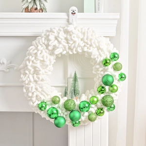 Chunky white knit Christmas wreath featuring assorted green ornaments on a white fireplace