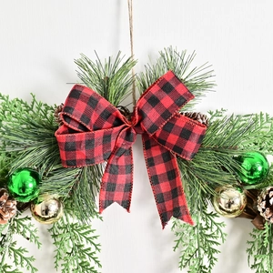 Christmas wreath with buffalo plaid bow, pine needles, and pinecones on white background