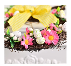 Detail of pink silk daisies and speckled eggs on a woven Easter wreath with yellow bow