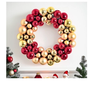 Detail of red and gold Christmas wreath with metallic and matte ornaments on white wall