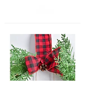 Close-up of red and black plaid bow and natural pine cone on a green Christmas wreath