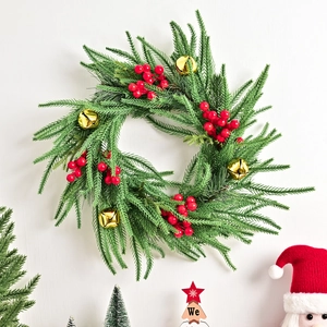 Christmas Norfolk Fir wreath with red berries and gold bells on a white wall