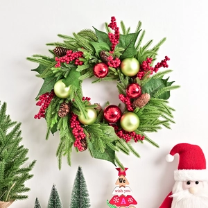 Ghirlanda di Natale con bacche rosse, pigne e ornamenti verdi appesa a una parete bianca