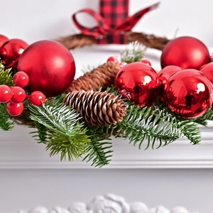 Christmas wreath with pine needles, red ornaments, cones and a plaid bow on white background