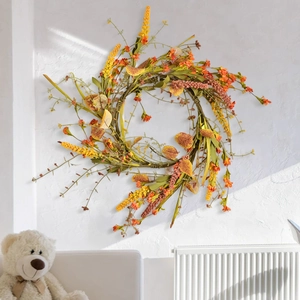 Autumn harvest wreath with yellow flowers and orange berries on a white textured wall