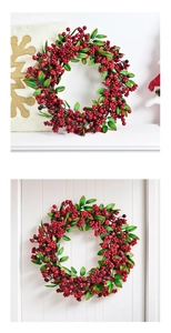 Close-up of artificial red berry wreath with green leaves on white wooden door and mantel