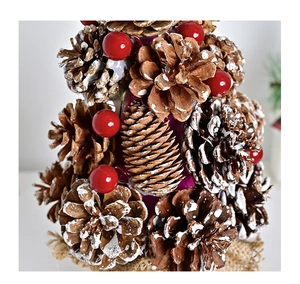 Close-up of mini pine cone Christmas tree with red berries and snowy burlap base