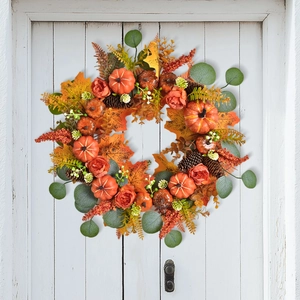 Autumn wreath with pumpkins and maple leaves hanging on a white wooden door decor