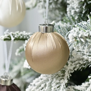 Champagne gold satin Christmas ball with vertical pleats hanging on a snowy tree