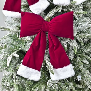 Large red velvet Christmas bow with white faux fur trim on a decorated pine tree