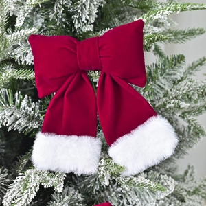 Large red velvet Christmas bow with white faux fur trim hanging on a snowy tree branch
