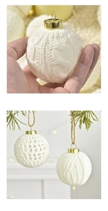 Detail einer weißen Strick-Weihnachtskugel mit Goldkappe am Kiefernzweig hängend
