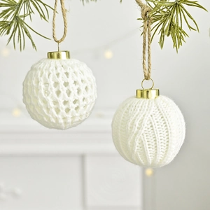Handgefertigte weiße Strick-Weihnachtskugeln mit Goldkappe an einem Kiefernzweig