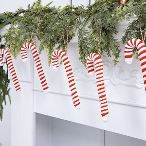 Red and white striped plush candy cane ornaments hanging on a festive green pine garland