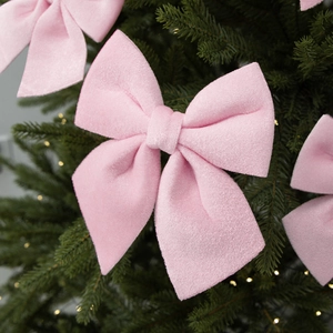 Pink velvet Christmas bow ornament hanging on a decorated tree with warm string lights
