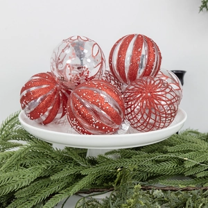 Red and white Christmas ornaments set with glitter on a white tray with pine branches