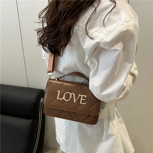 Sac bandoulière cylindre matelassé marron avec lettres LOVE dorées porté par un mannequin