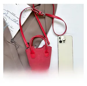 Dettaglio mini borsa a secchiello rossa con testo moda accanto a uno smartphone di scala