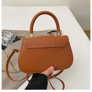 Detail of caramel brown leather crossbody bag with curved handle and gold hardware links