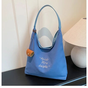 Detail of blue canvas tote bag with leather handles and artistic lettering on a table