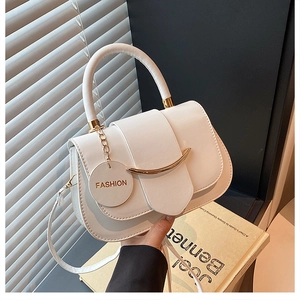 Close-up of white saddle bag with golden metal trim and a FASHION brand tag detail