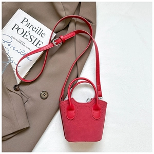 Mini borsa a secchiello in camoscio rosso con tracolla su sfondo di abito marrone