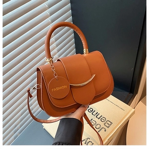 Detail view of brown faux leather handbag with gold metal bar and adjustable strap