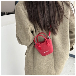 Dettaglio mini borsa a secchiello rossa in pelle scamosciata con scritta su modella in tweed