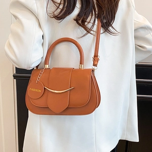 Brown leather crossbody bag with gold hardware and curved flap worn by a model in a suit