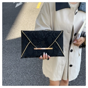 Détail d'une pochette enveloppe noire à texture serpent et finitions dorées chic