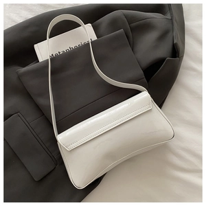 Détail d'un sac baguette en cuir verni blanc posé sur un blazer gris foncé chic
