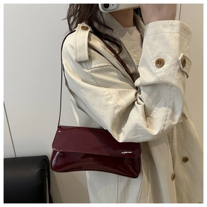 Gros plan d'un sac baguette en cuir verni bordeaux porté avec un trench-coat élégant