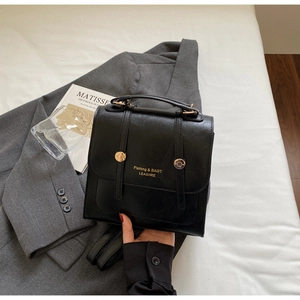 Detail of black vintage leather backpack with gold clasp on grey blazer and art book