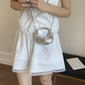 Detail of silver crescent bag with wave texture and chain strap on white dress