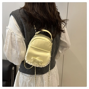 Detail of mini cream backpack with bow, lace trim bottom and metal chain strap on model