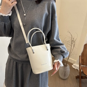 Minimalist white bucket bag with top handle and FASHION lettering in a cozy home setting