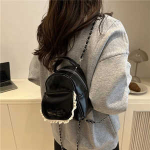 Mini black leather backpack with bow and lace detail shown on a model in a room