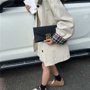 Pochette enveloppe noire tendance avec boucle dorée géométrique tenue par un mannequin