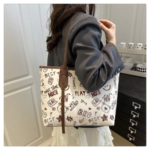 Detail of a graffiti print tote bag with brown straps styled on a model in a gray suit