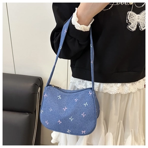Close-up of blue denim crescent bag with pink bow embroidery worn by a model