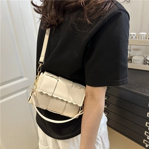 Sac bandoulière tissé blanc avec bords ondulés et chaîne dorée porté par un modèle