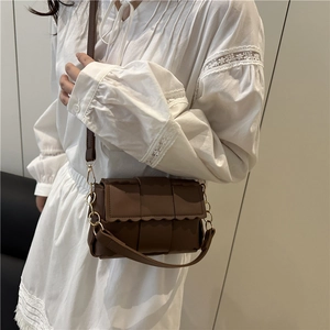 Sac bandoulière tressé marron foncé avec bords ondulés porté sur une robe en dentelle