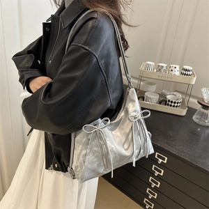 Silver metallic underarm bag with bow decoration and zipper detail shown on a model
