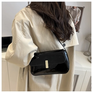 Detail view of stylish black patent leather shoulder bag with a silver metal buckle