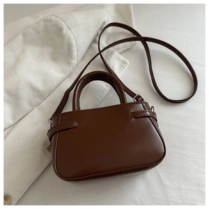 Detail of a brown PU leather handbag featuring cylindrical handles and side strap accents