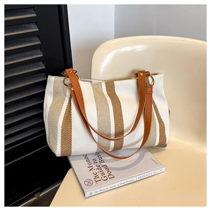 Detail of canvas tote bag with vertical stripes, leather straps, and gold ring hardware