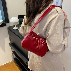 Red patent leather underarm bag with drawstring and silver eyelet details worn by a model