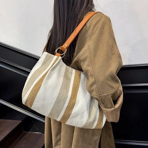 Vertical striped canvas tote bag with leather strap shown in a stylish over-the-shoulder view