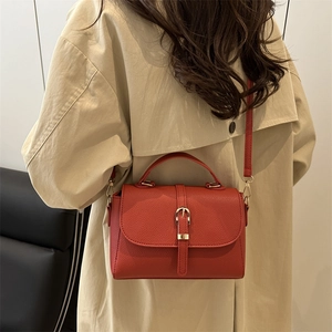 Sac à bandoulière rouge en cuir grainé avec boucle dorée sur trench-coat beige