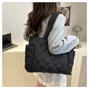 Detail of a large black quilted tote bag with diamond pattern worn by a model in office